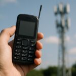 Dumbphone 4G tenu en main, antenne réseau mobile en arrière-plan